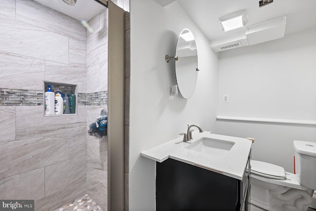 bathroom with visible vents, a tile shower, vanity, and toilet