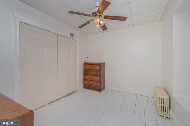 bedroom with a paneled ceiling, a closet, radiator, visible vents, and wood finished floors