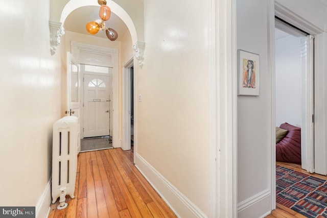 hall featuring arched walkways, light wood finished floors, radiator heating unit, and baseboards