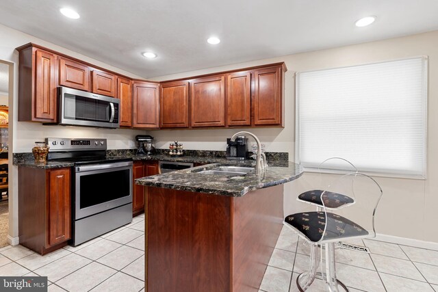 kitchen with dark stone countertops, a peninsula, light tile patterned flooring, stainless steel appliances, and a sink