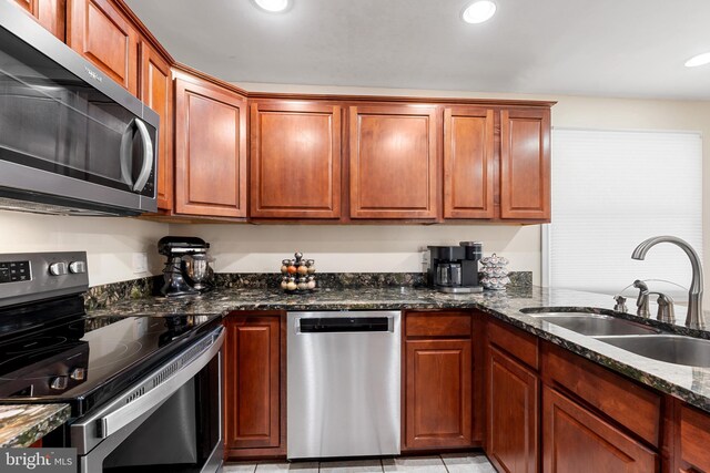 kitchen featuring dark stone countertops, recessed lighting, a sink, stainless steel appliances, and brown cabinets