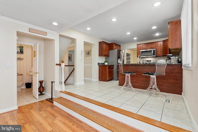 kitchen featuring a peninsula, light tile patterned flooring, recessed lighting, appliances with stainless steel finishes, and a kitchen breakfast bar