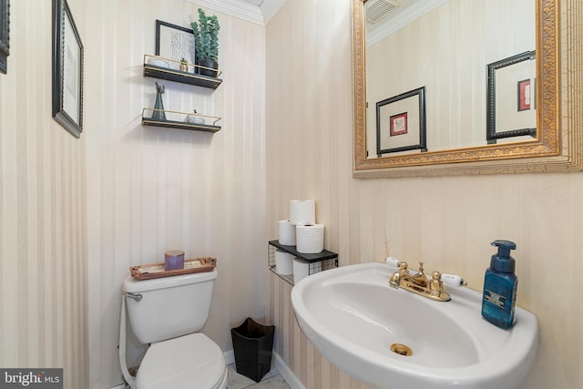 bathroom with visible vents, wallpapered walls, toilet, ornamental molding, and a sink