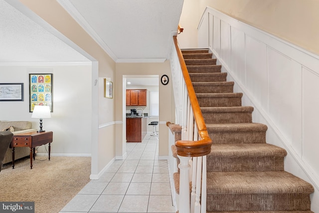 stairs with tile patterned flooring, a textured ceiling, crown molding, and carpet