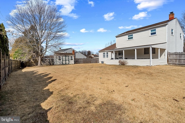 rear view of property with a shed, a lawn, a chimney, a fenced backyard, and an outbuilding