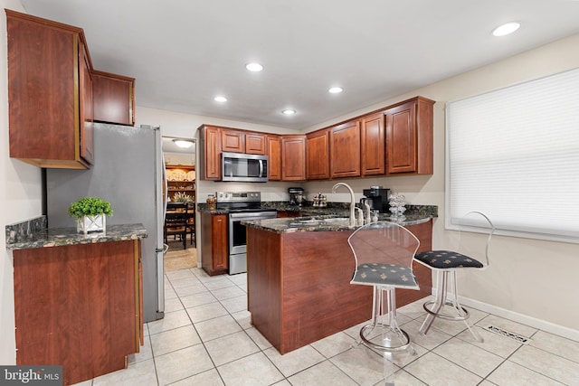 kitchen featuring light tile patterned flooring, dark stone countertops, appliances with stainless steel finishes, and a peninsula