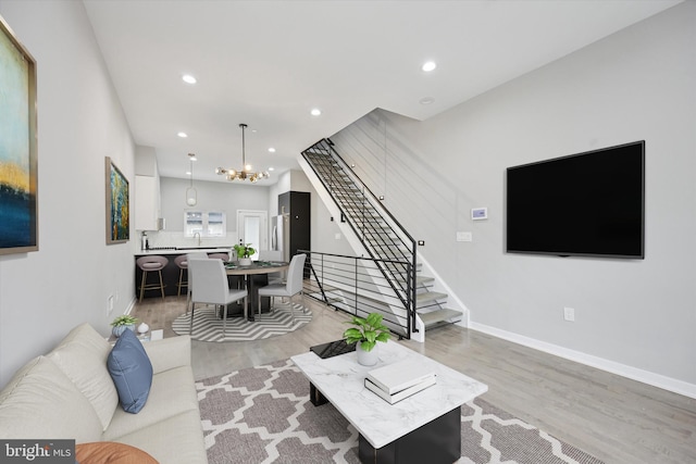 living room with recessed lighting, baseboards, stairs, light wood-type flooring, and an inviting chandelier