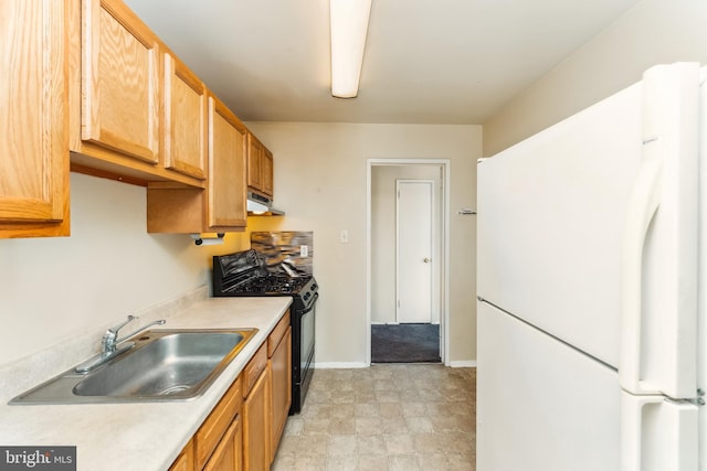 kitchen with light countertops, black gas range oven, freestanding refrigerator, a sink, and under cabinet range hood