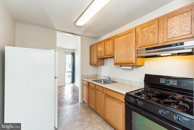 kitchen featuring under cabinet range hood, a sink, light countertops, freestanding refrigerator, and gas stove