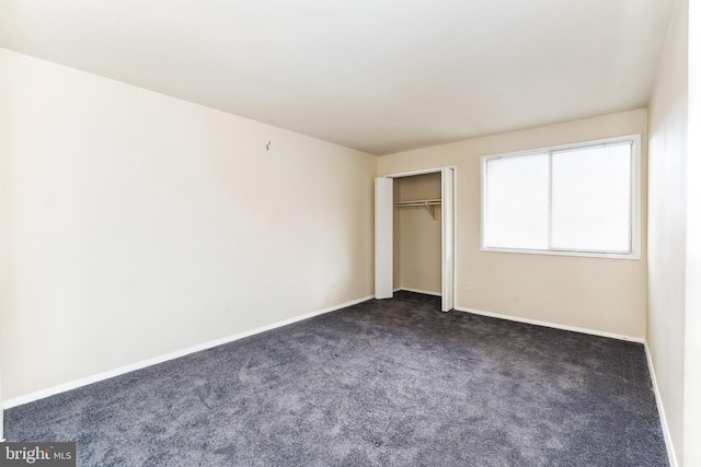 unfurnished bedroom featuring baseboards, dark carpet, and a closet