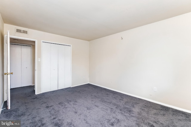 unfurnished bedroom featuring visible vents, dark colored carpet, and a closet