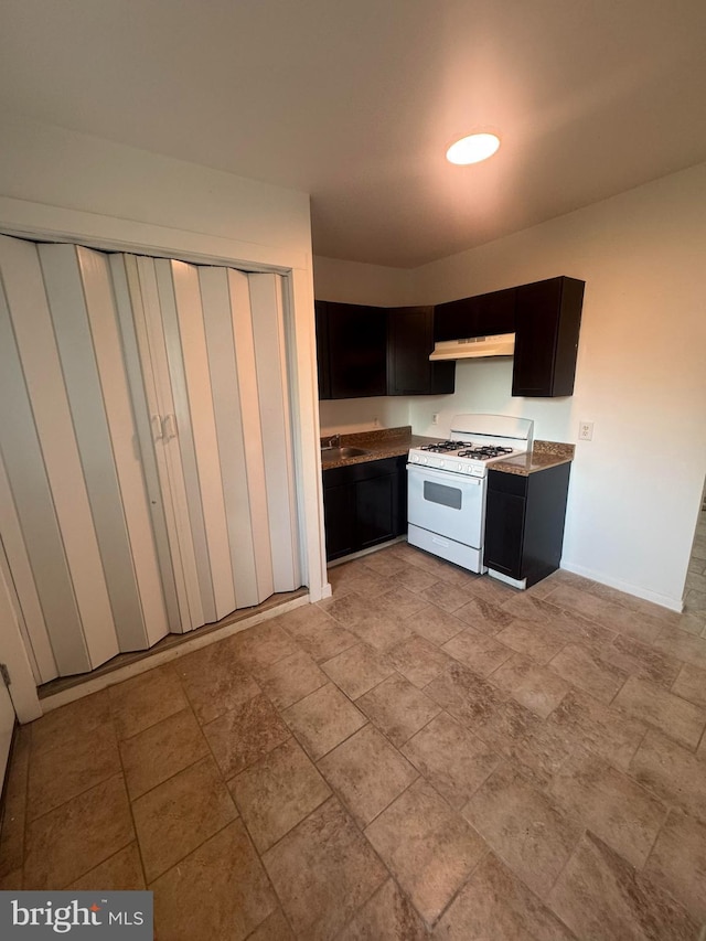 kitchen with baseboards, under cabinet range hood, a sink, and white range with gas stovetop