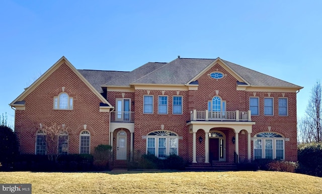 colonial-style house with brick siding, a front lawn, and a balcony
