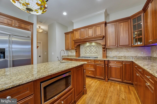 kitchen with light wood-style flooring, tasteful backsplash, light stone counters, a sink, and built in appliances