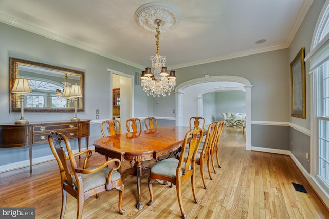 dining area with light wood-type flooring, an inviting chandelier, visible vents, and arched walkways