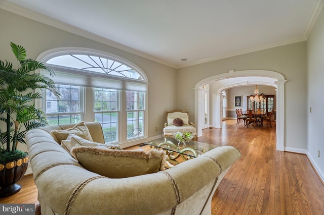 living area with decorative columns, arched walkways, wood-type flooring, baseboards, and a notable chandelier