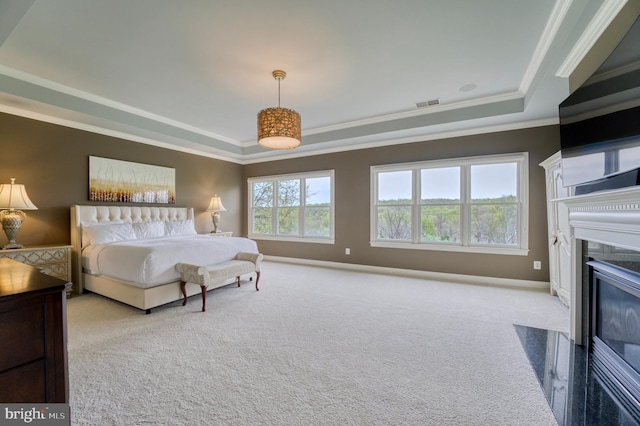 carpeted bedroom featuring a tray ceiling, a premium fireplace, ornamental molding, and visible vents
