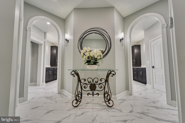 corridor with arched walkways, marble finish floor, and baseboards