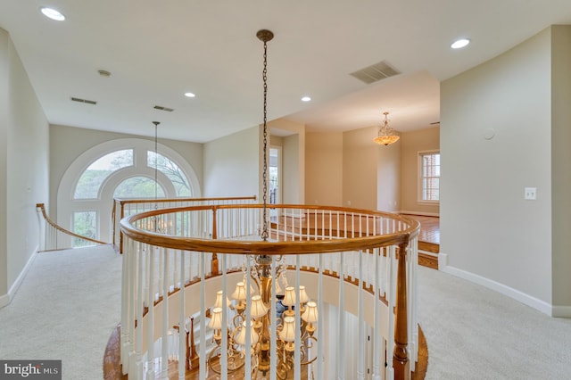 hall with visible vents, baseboards, an upstairs landing, and carpet flooring