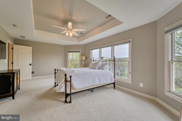 carpeted bedroom with a tray ceiling, baseboards, and visible vents