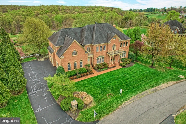 view of front facade featuring a garage, a forest view, a front lawn, brick siding, and driveway