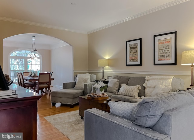 living room featuring light wood finished floors, a notable chandelier, arched walkways, and crown molding