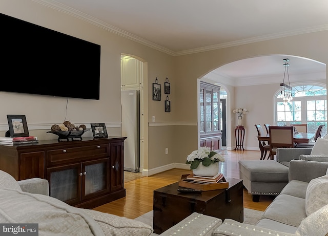 living room featuring a healthy amount of sunlight, light wood finished floors, ornamental molding, and a notable chandelier