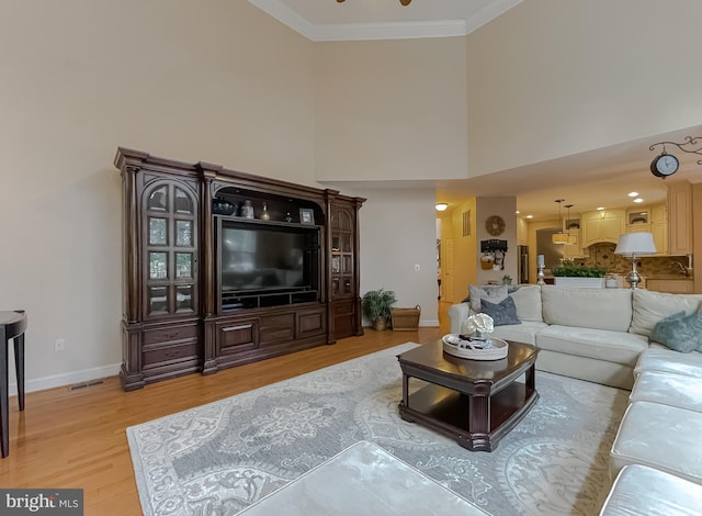 living area featuring crown molding, light wood finished floors, visible vents, a towering ceiling, and baseboards