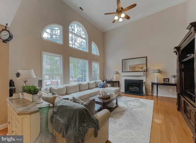 living area with a high ceiling, a fireplace with flush hearth, visible vents, light wood-style floors, and crown molding