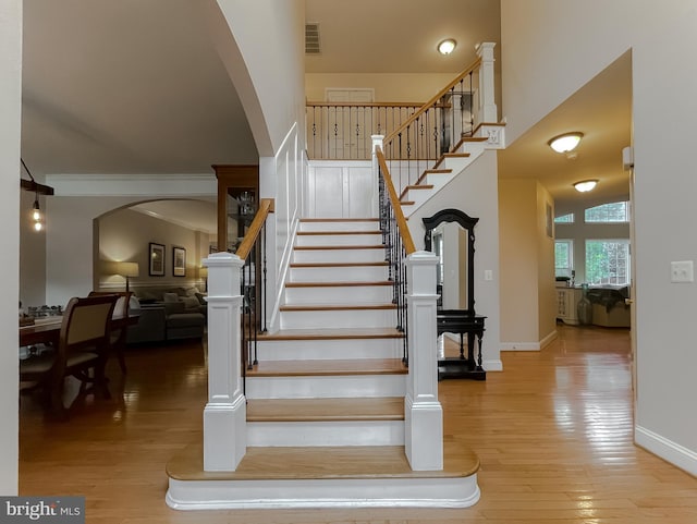 stairway with baseboards, visible vents, arched walkways, wood finished floors, and a high ceiling