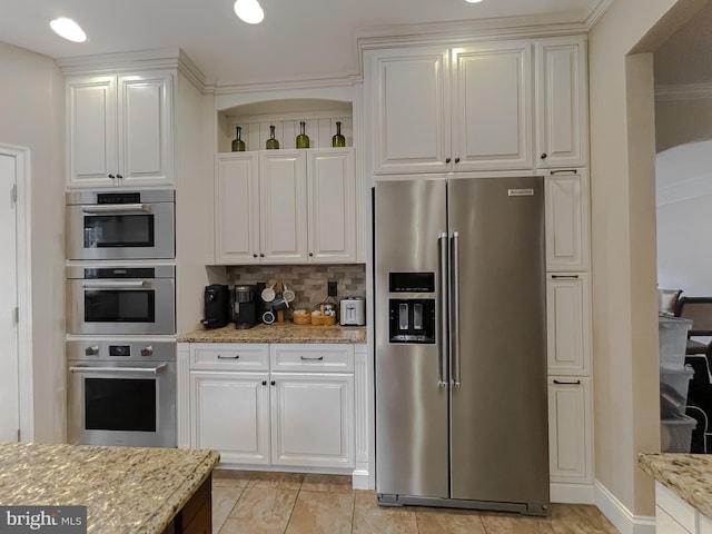 kitchen featuring stainless steel appliances, light stone countertops, white cabinetry, and tasteful backsplash