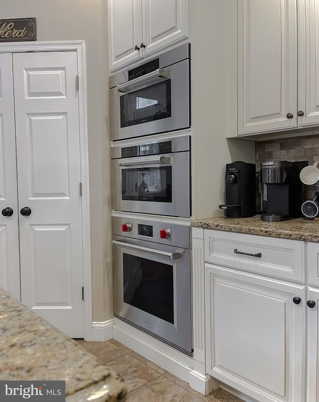 kitchen featuring double oven, white cabinetry, decorative backsplash, and light stone countertops