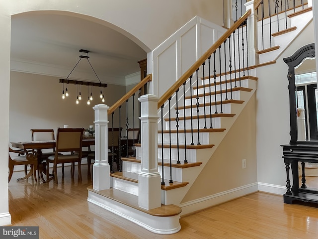 stairs with arched walkways, ornamental molding, wood finished floors, and baseboards