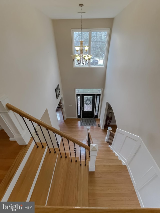 foyer with a decorative wall, a notable chandelier, wood finished floors, a towering ceiling, and stairs