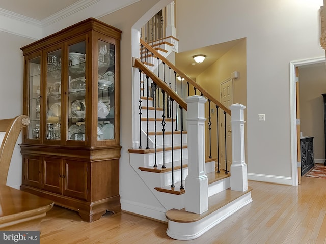 staircase with arched walkways, crown molding, baseboards, and wood finished floors