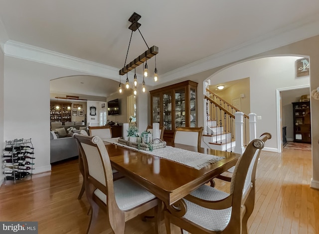 dining space featuring arched walkways, baseboards, light wood-style flooring, stairway, and ornamental molding