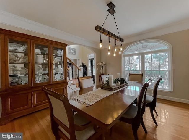 dining room featuring arched walkways, baseboards, stairs, ornamental molding, and light wood finished floors