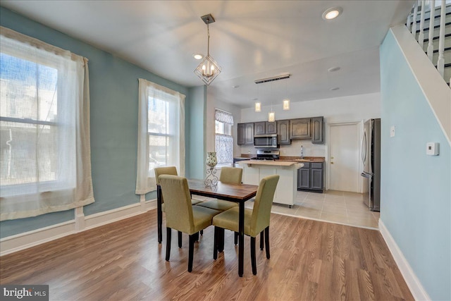 dining area featuring stairway, an inviting chandelier, light wood-style flooring, and baseboards