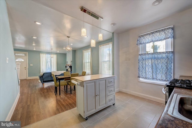 kitchen with light tile patterned floors, decorative light fixtures, a kitchen island, baseboards, and gas range