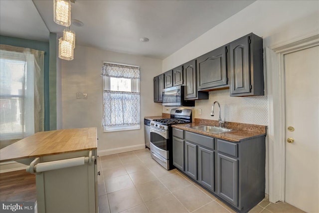 kitchen featuring light tile patterned floors, a sink, baseboards, appliances with stainless steel finishes, and decorative backsplash