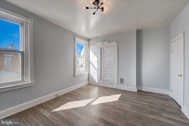 unfurnished bedroom with visible vents, baseboards, a chandelier, and wood finished floors