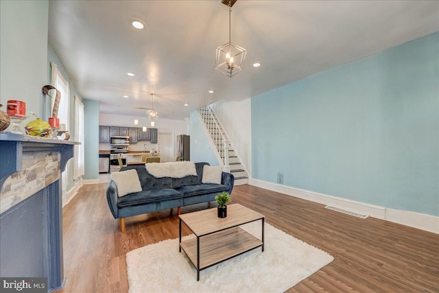 living room with a stone fireplace, stairway, baseboards, and wood finished floors