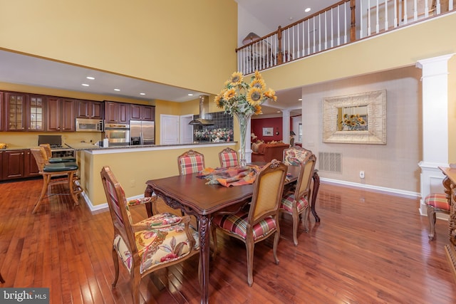 dining space with baseboards, hardwood / wood-style flooring, visible vents, and ornate columns