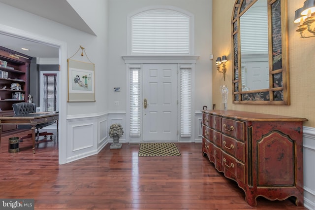 foyer entrance featuring dark wood-style floors, a decorative wall, and a wainscoted wall