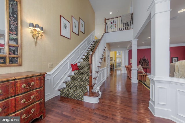 stairway with a decorative wall, recessed lighting, wood finished floors, wainscoting, and ornate columns