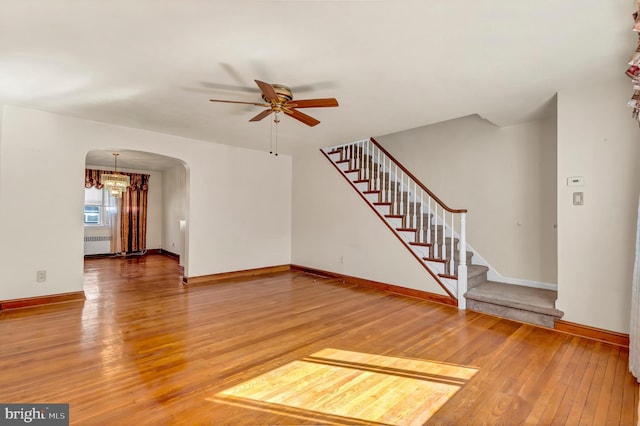 unfurnished living room featuring baseboards, arched walkways, radiator, hardwood / wood-style flooring, and stairway