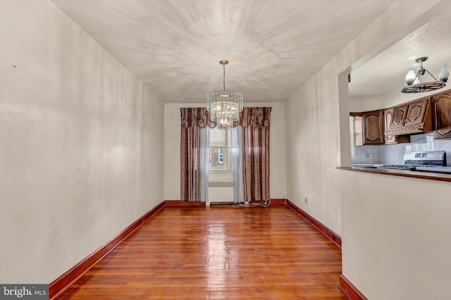 unfurnished dining area featuring radiator, a notable chandelier, baseboards, and wood finished floors