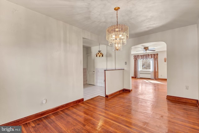 empty room featuring a ceiling fan, wood-type flooring, arched walkways, and baseboards