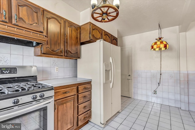 kitchen with a textured ceiling, stainless steel gas range oven, under cabinet range hood, white refrigerator with ice dispenser, and light countertops