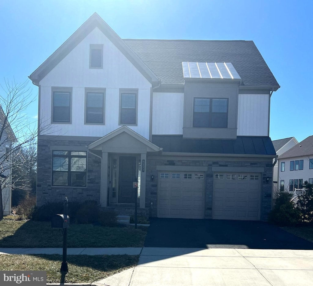 view of front facade with driveway, a garage, stone siding, metal roof, and a standing seam roof